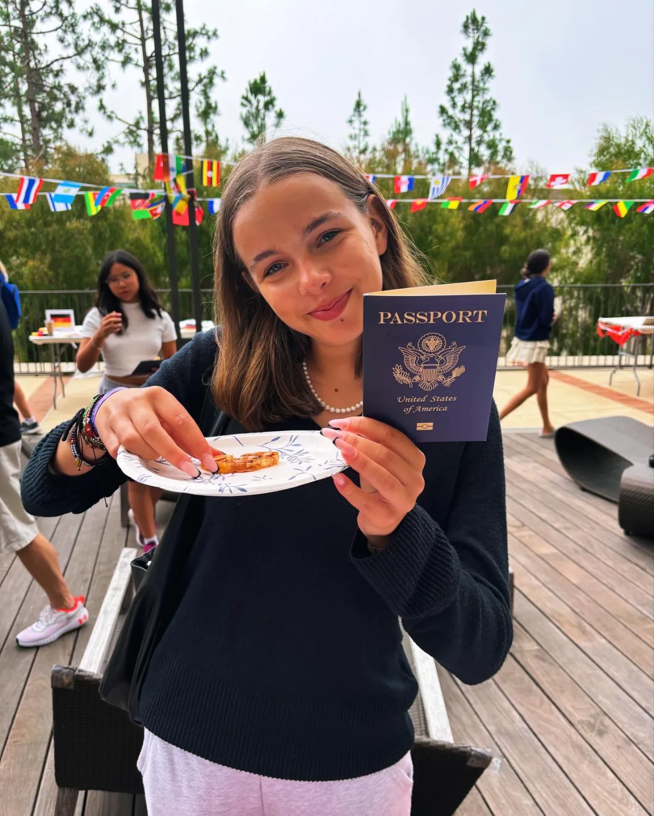 A student holding a passport and a plate of food at ELC culture day, under international flag bunting