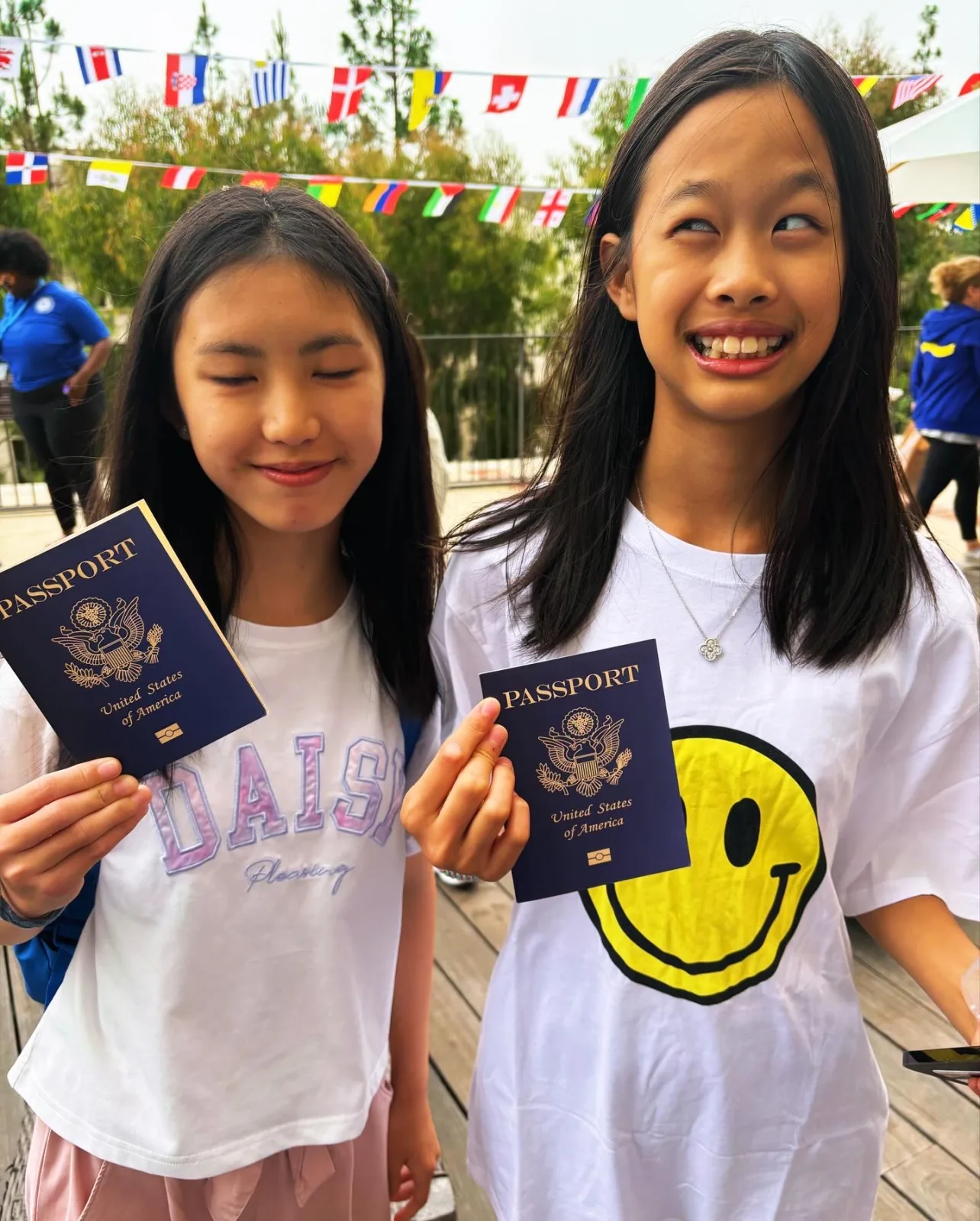 Two students holding passports at ELC culture day at UCLA, with flags of many countries strung overhead