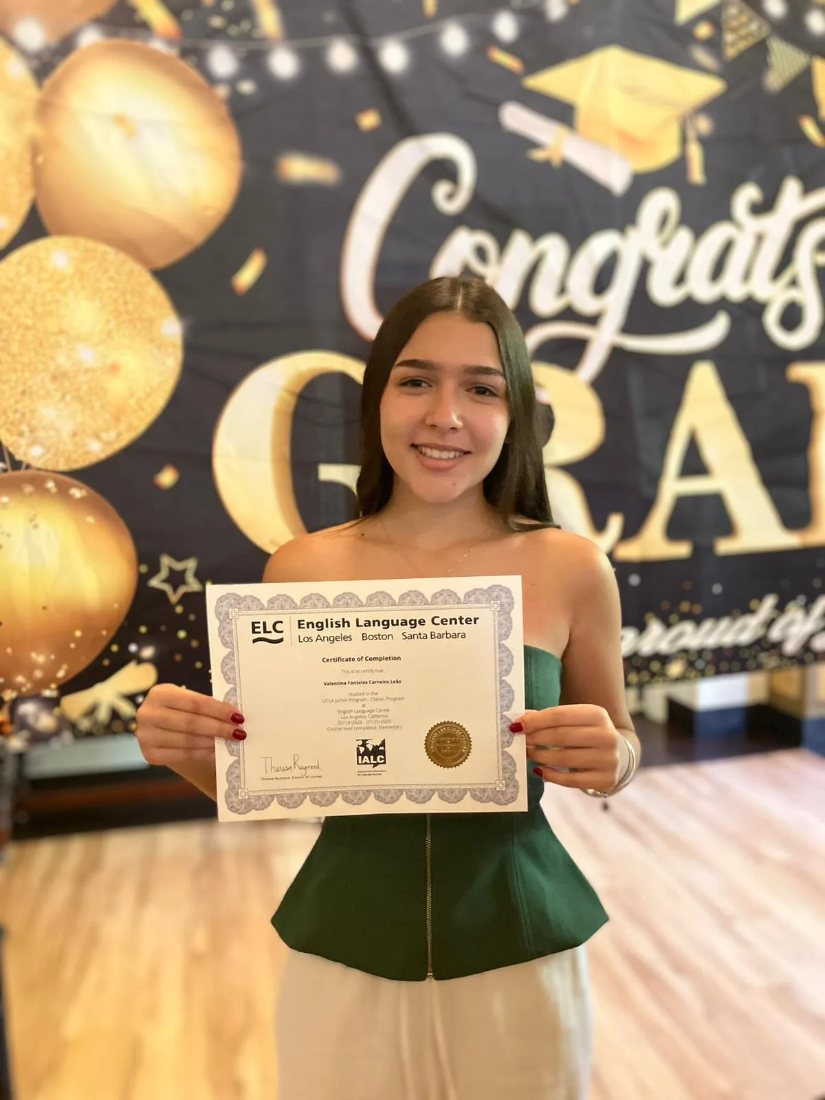A student holding an ELC certificate of completion in front of a Congrats Grad backdrop at UCLA